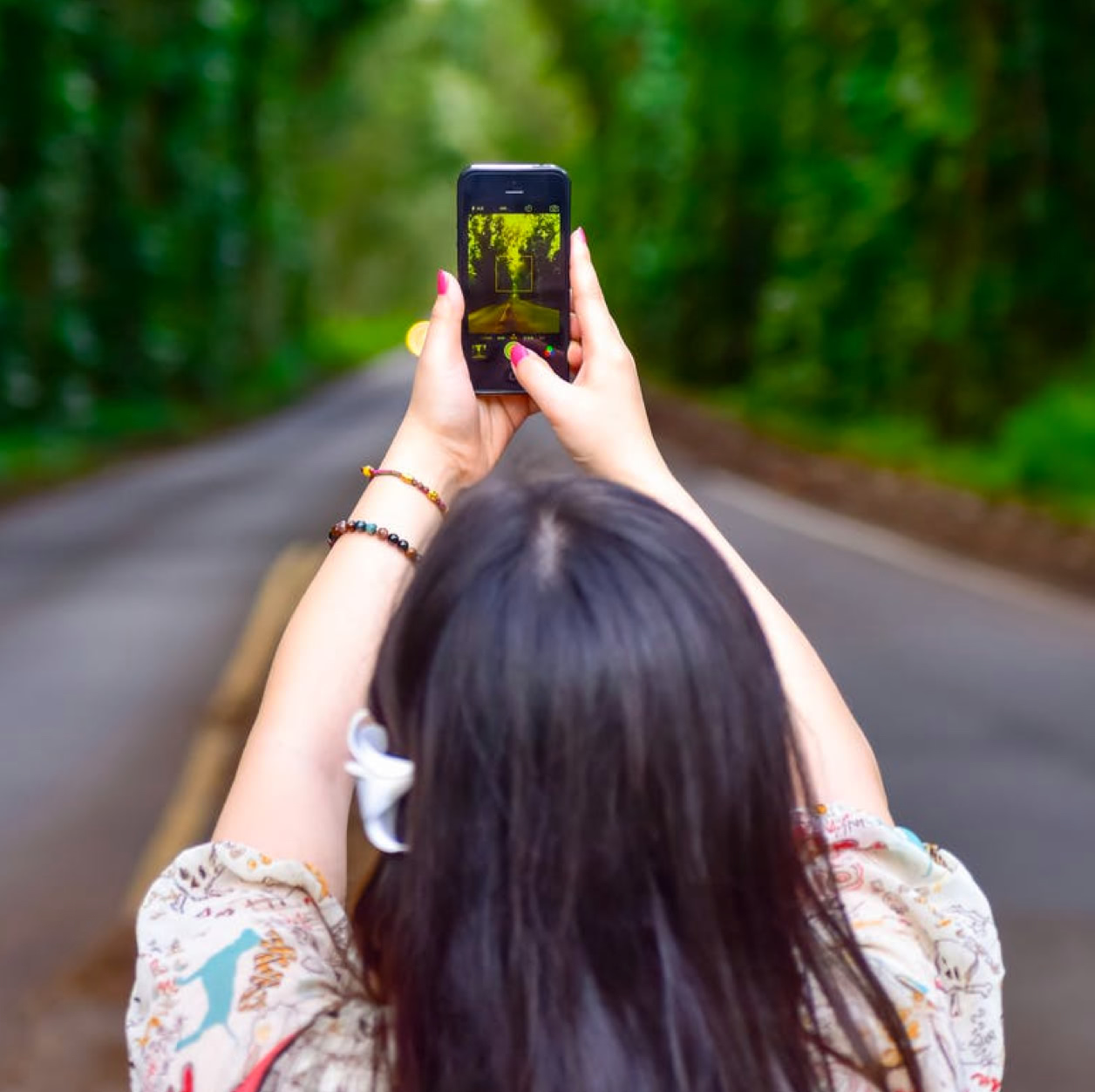 Femme de dos prenant une route en photo avec un smartphone.